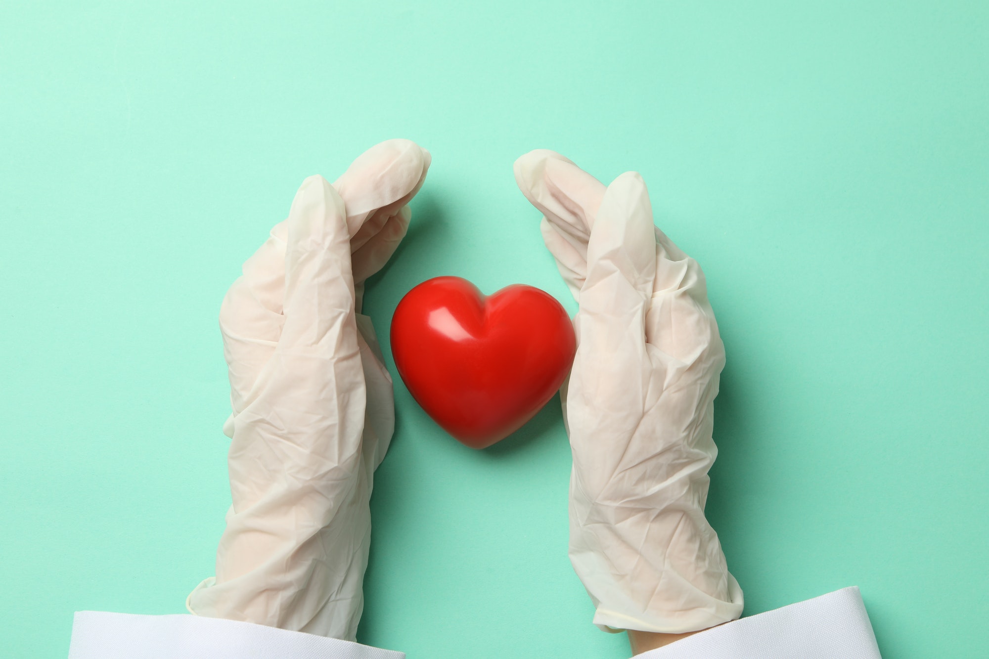 Female doctor hands in gloves and heart on mint background