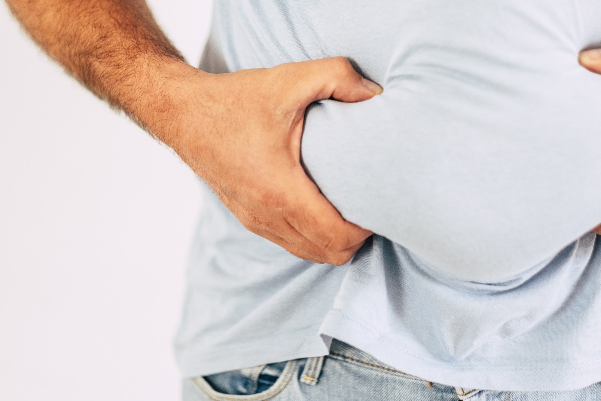 Close up of caucasian man's hand holding belly abdominal fat - concept of junk food and diet